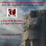 Stone monument of civil rights leader, Rev. Dr. Martin Luther King, Jr. with folded arms against a cloudy sky, overlaid with text announcing Caldwell Law is closed for MLK Day.